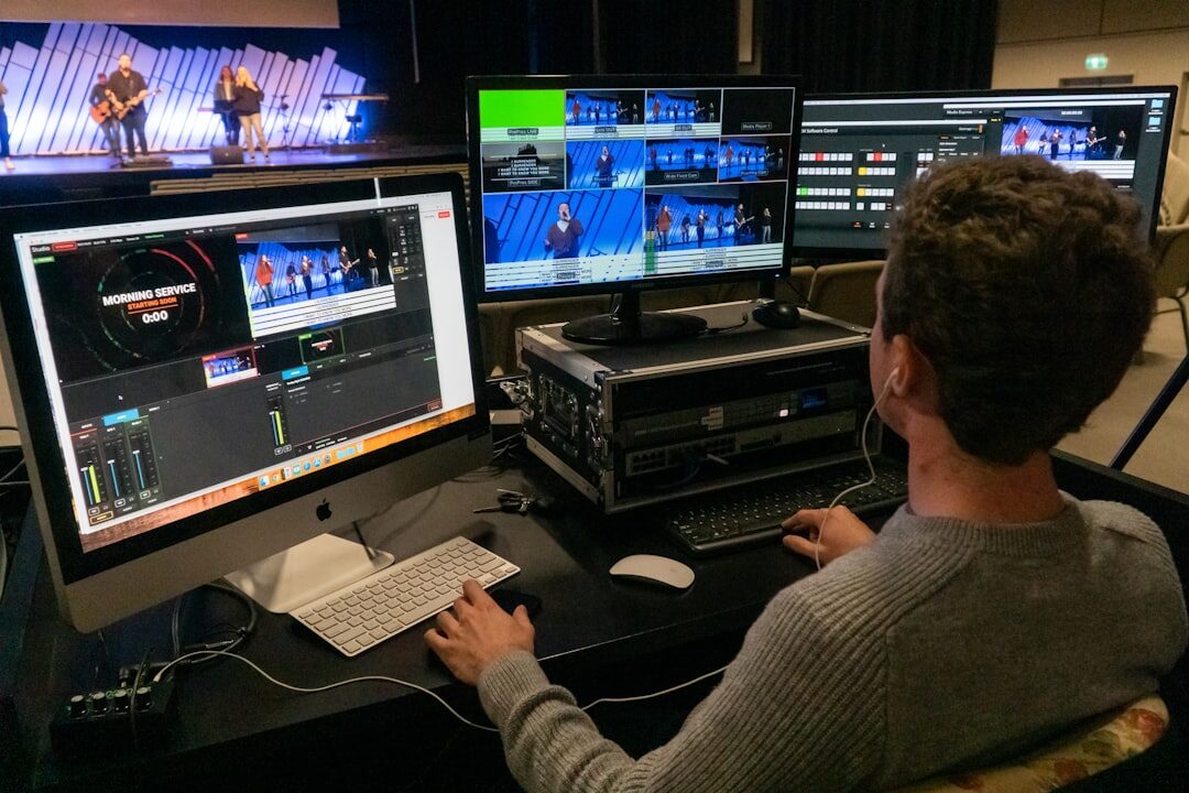 Editor reviewing broadcast footage on a laptop with reference monitors in the background
